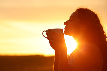 Silhouette of a woman smelling coffee at sunset
