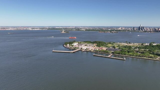 An aerial view of New York harbor on a sunny day with clear blue skies. The drone camera truck left then zoom in over the water, high enough to see Governors Island and New Jersey in the background.