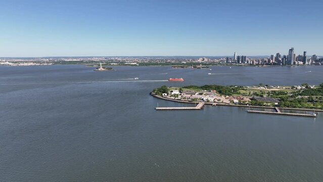 An aerial view of New York harbor on a sunny day with clear blue skies. The drone camera truck left over the water, high enough to see Governors Island and New Jersey in the background.
