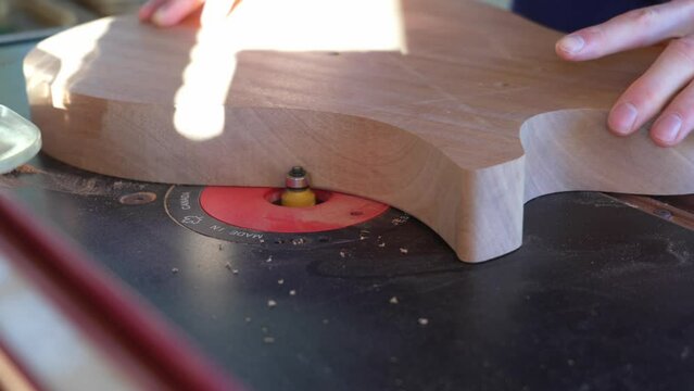 Guitar maker rounding over edges of guitar body made of mahogany wood. Electric resonator guitar building process