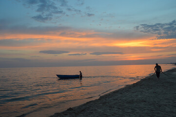 Silhouette of a boat near the shore against the background of the setting orange sun