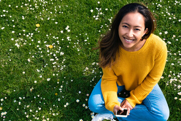 Happy young woman with smart phone sitting at park