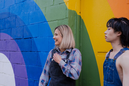 Happy young woman standing by friend in front of rainbow mural