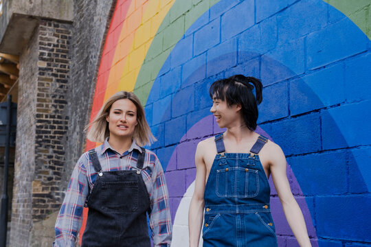 Young friends walking together by rainbow painted on wall