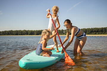 Girls with mother on stand up paddle board amidst lake