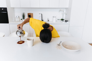 Exkausted woman spilling coffee on kitchen table