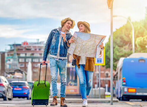 Young man with luggage walking with woman holding map on vacation