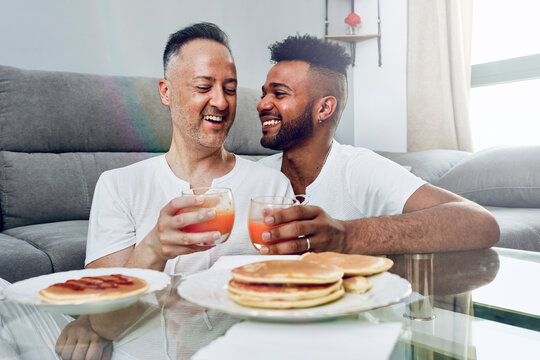 Happy gay couple having breakfast in living room at home