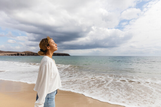 Woman with eyes closed standing by sea at beach