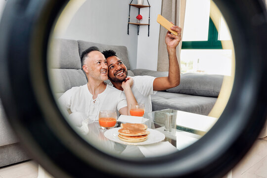 Happy couple taking selfie seen through ring light at home