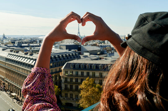 Young woman making heart shape with hands in front of Eiffel Tower, Paris, France
