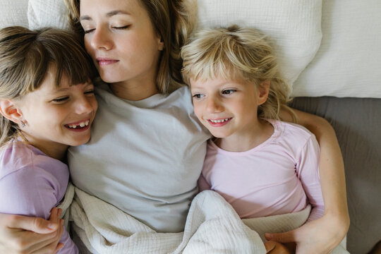 Smiling siblings relaxing with mother in bed at home