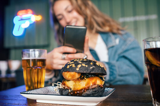 Young woman photographing burger through smart phone at restaurant