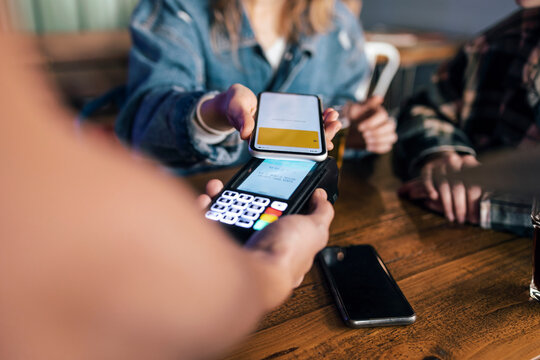 Young woman paying bill through smart phone at restaurant - Powered by Adobe