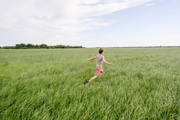 Boy running at green grass field by sky
