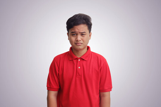 Portrait of unpleasant Asian man in red polo shirt showing his face sadness. Isolated image on gray background