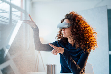 Young engineer with curly hair wearing virtual reality simulator sitting at office