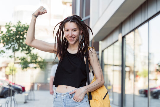 Smiling non-binary person with hand in pocket flexing muscle