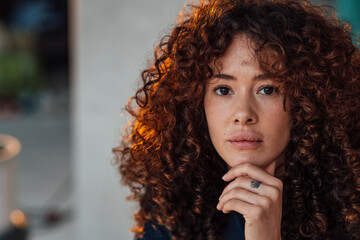 Curly haired beautiful young woman with hand on chin