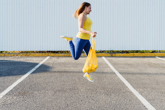 Woman jumping on road holding mesh bag with lemons
