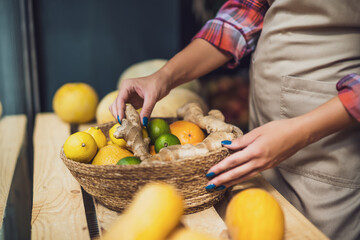 Woman works in fruits and vegetables shop. She is stacking goods in storefront.
