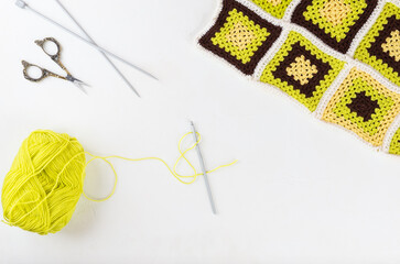 Hook with threads for knitting, scissors and knitting needles on a light table.
