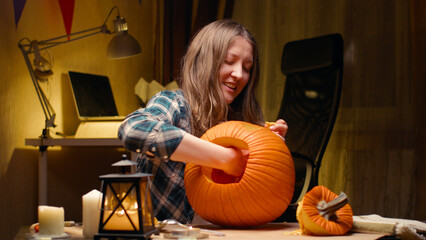 Preparing pumpkin for Halloween. Woman sitting and pulling out face details of carved halloween Jack O Lantern pumpkin at home for her family.