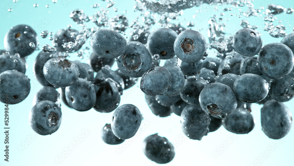 Aufkleber Blueberries pieces falling underwater on blue background.