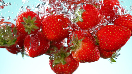 Strawberries pieces falling underwater on white background.