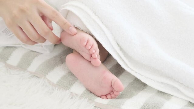 Mother plays with foot of her sleeping baby.