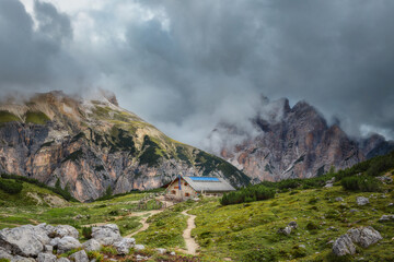 Fototapeta na wymiar Mystical beautiful landscape with rocky mountains and beautiful mountain house in the fog in cloudy weather, Italian alps. Tre Cime park in Dolomites, Italy