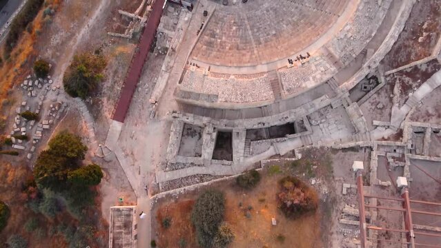 Aerial drone footage of archaeological site of ancient Kourio in Limassol district, Cyprus. Top down view of the theatre forming a semicircle, tilt to greek roman ruins and beach at sunset from above.