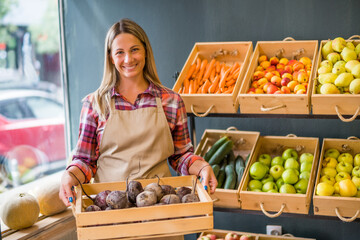 Woman works in fruits and vegetables shop. She is holding basket with beetroot.