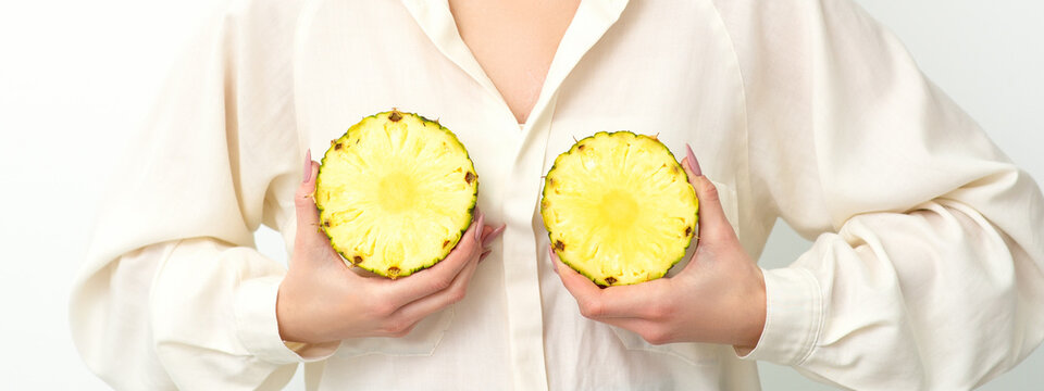 Young Caucasian smiling woman holding slices pineapple over white background, breast health concept