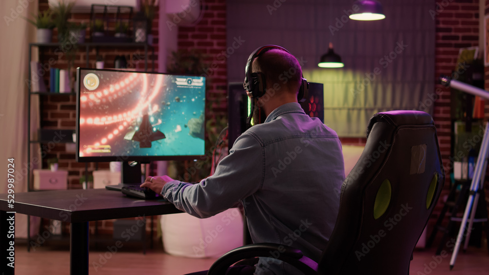 Poster over shoulder view of caucasian man using pc setup playing multiplayer online action game talking to