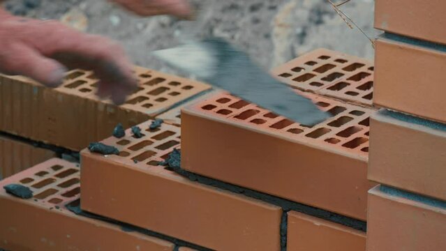 Working bricklayer lays brick on cement mortar. Building brick wall or fence.