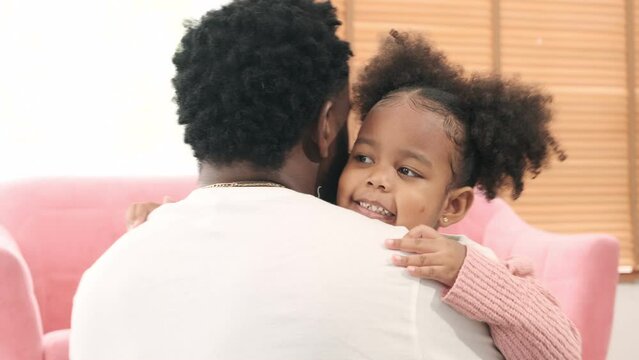 Black father hugging his daughter who ran in come hug in living room.