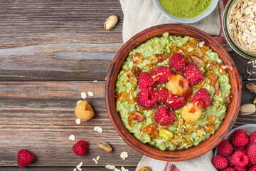 Oatmeal matcha porridge with fresh raspberries, caramel sauce and pistachios in a bowl on rustic wooden table. Top view