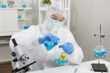 Male Scientist in PPE Suit working in Lab while Pouring Solution from Cylinder to Erlenmeyer Flask...