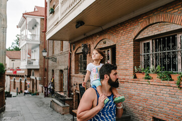 Young father walking with little daughter outdoors, on streets in city of Tbilisi in the capital of Georgia on sunny spring day. Dad and girl travel on excursion in old town.