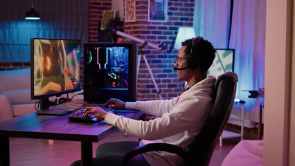 African american gamer playing online multiplayer game celebrating after winning online competition on gaming pc at home. Man doing victory hand gesture happy after win in first person shooter. © DC Studio