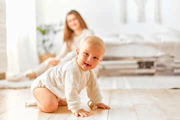 A cheerful baby crawls on the floor and laughs at the camera, with mom in the background.
