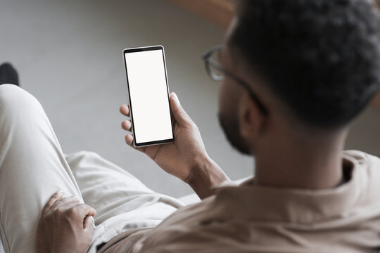 Smartphone mockup. Close up of young man hand holding black phone with white blank screen at home. Isolated on white background. Mobile phone frameless design concept