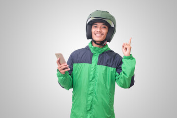 Portrait of Asian online taxi driver wearing green jacket and helmet holding mobile phone and pointing to empty space with finger. Isolated image on white background