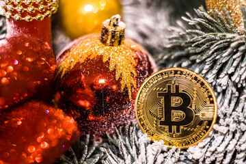 Christmas decorations, red balls and golden souvenir crypto currency Bitcoin on decorative New Year tree branch.