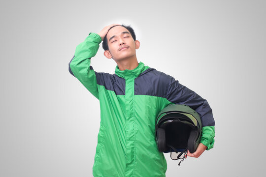 Portrait of Asian online taxi driver wearing green jacket straightening his hair and holding helmet. Isolated image on white background