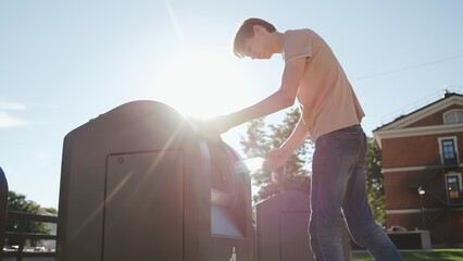 Young man throw away an empty plastic bottle into a trash bin outdoors