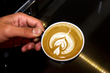 Closeup image of a hand holding a white cup of hot coffee