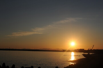 Sunset with a clear sky and sunlight reflexing on the surface of an ocean in the evening at the beach at the sea in fishing town in summer in Japan