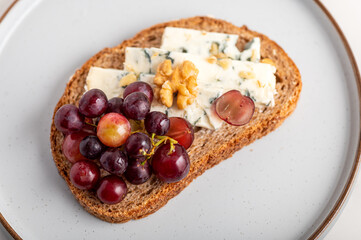 Toasted bread with mild creamy blue cheese, grapes and walnuts on grey plate